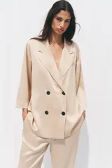 Blazer color beige de cuello solapa y manga tres cuartos. Tejido con efecto arrugado y cierre frontal cruzado con botones negros.