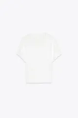 Camiseta blanca de algodón con cuello redondo y manga corta. Presenta bordados florales a tono en el lateral derecho del pecho y en la parte inferior izquierda.