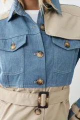 Trench largo color beige con secciones en denim azul, cuello camisero, cierre frontal con botones y bolsillos con solapa en el pecho.
