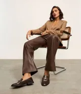 Zapato mocasín de cuero color marrón oscuro con detalle metálico dorado en la parte delantera.