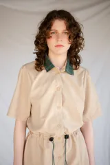 Vestido corto verde militar de microfibra con cuello camisero negro, cintura elastizada con cordón de ajuste y mangas cortas con dobladillo. Cierre frontal con botones.