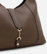 Cartera tipo hobo grande de color marrón oscuro, confeccionada en PU (poliuretano) con textura que imita cuero granulado. Presenta un asa de mano y un detalle de tira con hebilla metálica en la parte frontal superior.