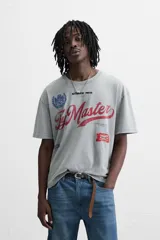 Camiseta gris con cuello redondo y manga corta. Presenta estampados, bordados y parches frontales combinados a contraste. Tiene un efecto lavado.