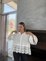 Camisa blanca de lino con cuello clásico, cierre frontal con botones, mangas 3/4 acampanadas con detalle de puntilla calada y ruedo con volados y puntilla calada.