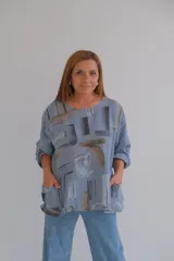 Blusa celeste con estampado abstracto en tonos grises y marrones, de corte holgado, mangas largas con puños abotonados y bolsillos delanteros.