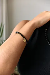 Pulsera elástica de piedras naturales color marrón con dije circular dorado con la palabra "AIRE" grabada.