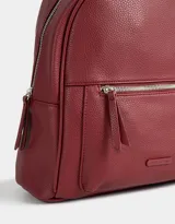 Mochila negra de cuerina con bolsillo frontal con cierre, correas regulables, manija superior, cierre superior y tag de metal.