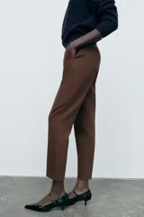 Pantalón marrón de tiro alto con costuras marcadas en delantero y espalda, bolsillos delanteros de vivo y cierre frontal con cremallera, botón interior y gancho metálico.