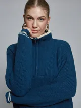 Sweater color crema de tejido grueso con medio cierre, cuello alto y detalles deportivos con rayas negras en puños y hombros.