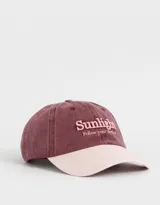 Gorra de gabardina color borgoña con visera rosa claro. Tiene bordado en relieve con la palabra "Sunlight" y la frase "Follow your destiny" en rosa.