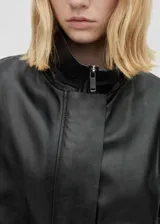 Abrigo negro oversize de cuero ovino con cuello alto y cierre frontal con cremallera y botones ocultos.