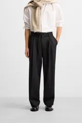 Pantalón negro de corte ancho con cinturón de tela con hebilla metálica y pliegues frontales.