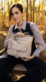 Cartera color beige con apertura superior con cierre, bolsillo frontal con tapa y detalle de trenza artesanal, división al medio y bolsillos internos, bolsillitos laterales tipo ojal, bolsillo con cierre atrás y correa larga regulable.