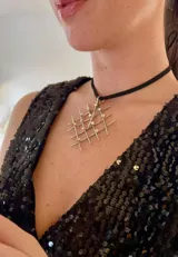 Collar con dije plateado de forma geométrica con incrustaciones de strass y tira de terciopelo negro.