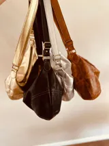 Cartera plateada tipo banana bag de cuero, con correa ajustable y cierre superior.