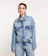 Campera de jean celeste, corte cropped y holgado, con cuello camisero, cierre abotonado, mangas largas, bolsillos con solapa en el pecho y recortes verticales.