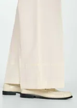 Pantalón de vestir color crema, de corte recto y largo, con pinzas delanteras, bolsillos laterales y trabillas.