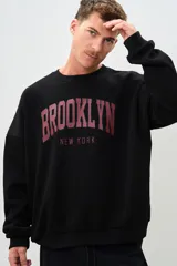Buzo negro de corte holgado con estampa frontal de letras en color borgoña que dice "BROOKLYN" y "NEW YORK".