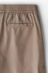 Pantalón cargo color beige de corte recto, con cintura elástica ajustable con cordón, bolsillos laterales con cierre, bolsillos tipo cargo con solapa en los laterales y bolsillos traseros insertados.