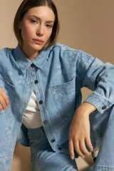 Sobrecamisa de denim celeste con estampado floral tono sobre tono. Presenta cuello camisero, cartera frontal con botones metálicos y bolsillos aplicados en el pecho.