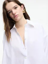 Camisa blanca de algodón con cuello camisero y cierre frontal con botones.