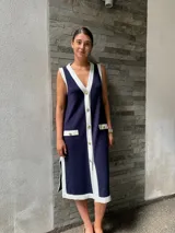 Vestido tipo chaleco azul marino con ribetes blancos, cuello en V, botones dorados y bolsillos frontales.