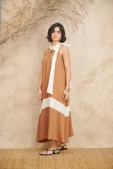 Vestido largo color marrón con corte debajo del busto y falda acampanada. Presenta cuello halter con lazo blanco.