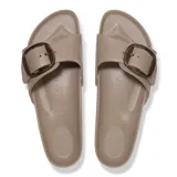 Sandalia tipo pantufla de una sola tira ancha, color topo grisáceo, fabricada en EVA. Presenta una hebilla grande y prominente de color cobre o bronce.