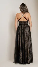 Vestido largo de fiesta con escote profundo en V, confeccionado en encaje negro sobre una base color piel y tul negro. Tiene breteles finos y falda con tajo alto.