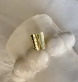 Anillo abierto dorado con dos rectángulos texturados en los extremos.