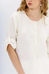 Vestido midi tipo túnica color blanco, de lino y algodón. Tiene calce recto, escote redondo con botones y bordados en hilo en el frente, sisas y ruedo.