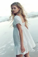 Vestido corto blanco de tejido liviano con escote corazón, mangas cortas abullonadas y elástico fino en hombros y puños. Espalda fruncida y corte ajustado en el busto con costura fruncida debajo. Pollera con leve vuelo y costura fruncida en el bajo.