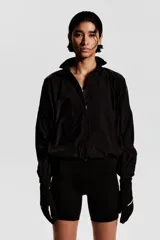 Campera negra de nylon repelente al agua y rompevientos con cuello elevado, cierre con protección para el mentón y bolsillos laterales con cierre. Modelo con hombros caídos, orificios de ventilación en las sisas y mangas murciélago con puños elásticos. Panel de ventilación en malla en la parte baja de la espalda y cordón para ajustar elástico con topes en el bajo. Forro de malla.