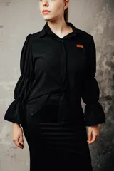 Camisa negra de algodón con cuello clásico, mangas largas abullonadas con puños elásticos y cierre frontal con botones.