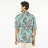 Camisa celeste con estampado de hojas de palmera en tonos negro y blanco, de corte recto, con cuello cubano y mangas cortas con dobladillo.