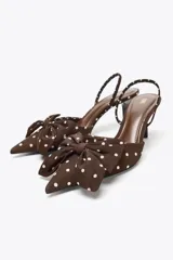Zapato de tacón marrón con estampado de lunares blancos, tira trasera con elástico, punta fina y detalle de lazo en la parte delantera.