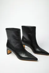 Bota en punta con caña ancha de símil cuero charol, con taco medio y suela de goma.