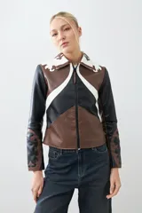 Chaqueta corta de cuero sintético color negro, marrón y blanco, con cuello de piel sintética blanca, cierre frontal con cremallera y bordados en las mangas.
