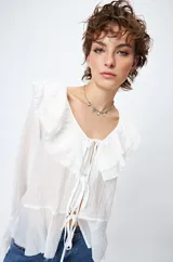 Blusa blanca de gasa con escote en V y volados en el cuello y las mangas largas. Se ata con lazos finos al frente.