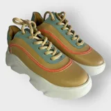 Zapatillas urbanas color mostaza, con detalles en verde menta y naranja. Confeccionadas en cuero sintético con cordones beige y suela de plataforma blanca.