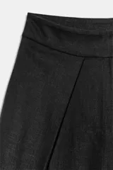 Pantalón wide leg negro de tiro medio confeccionado en hilatura con lino. Presenta bolsillos laterales ocultos en costura, detalle de pinzas en delantero y cierre frontal con cremallera, botón y ganchos metálicos.