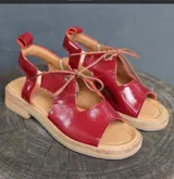 Sandalias rojas de cuero charol con puntera descubierta y cierre con cordones finos.