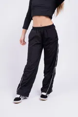 Pantalón negro de acetato con cintura elástica y cordón ajustable. Presenta una franja blanca a lo largo de la pierna.