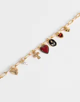 Collar corto dorado con cadena de eslabones grandes y dijes colgantes: corazones dorados, corazón rojo con borde dorado, cruz dorada, perla blanca y dije ovalado negro con detalle de strass.