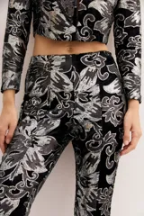 Pantalón de terciopelo negro con estampado floral plateado, corte acampanado y tiro alto.