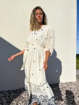 Vestido largo blanco con bordados azules, escote en V, mangas 3/4 abullonadas y lazo en la cintura.