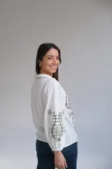 Camisa blanca de manga larga con elástico en puños, cuello mao con botones en la parte delantera y bordados florales en verde.