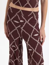 Pantalón de punto color marrón oscuro con estampado de cadenas y labios en color beige. Es de tiro alto, corte amplio y pierna recta, con cintura elastizada.