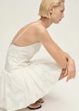Vestido corto blanco con textura, tirantes finos y espalda abierta con lazo. Tiene escote de pico, cierre de cremallera en la parte posterior y corte globo.