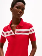 Chomba roja de piqué de algodón elástico con corte slim, cuello clásico, tapeta de seis botones y rayas horizontales blancas en el pecho y mangas. Logo de Tommy Hilfiger bordado en la manga.